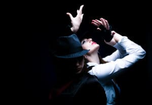 Two individuals, striking dramatic poses while wearing the Porro Neque Quisq black hats and dark clothing, are set against a black background, with one gazing upward and the other looking downward.