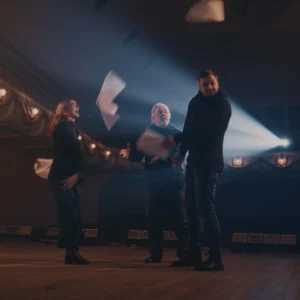 Three individuals on a dimly lit stage toss papers into the air, highlighted by a spotlight shining behind them, showcasing the Neque Porro Quisq.