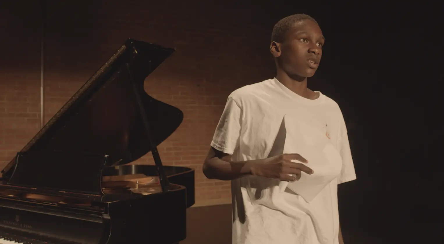 Young man holding paper beside grand piano.