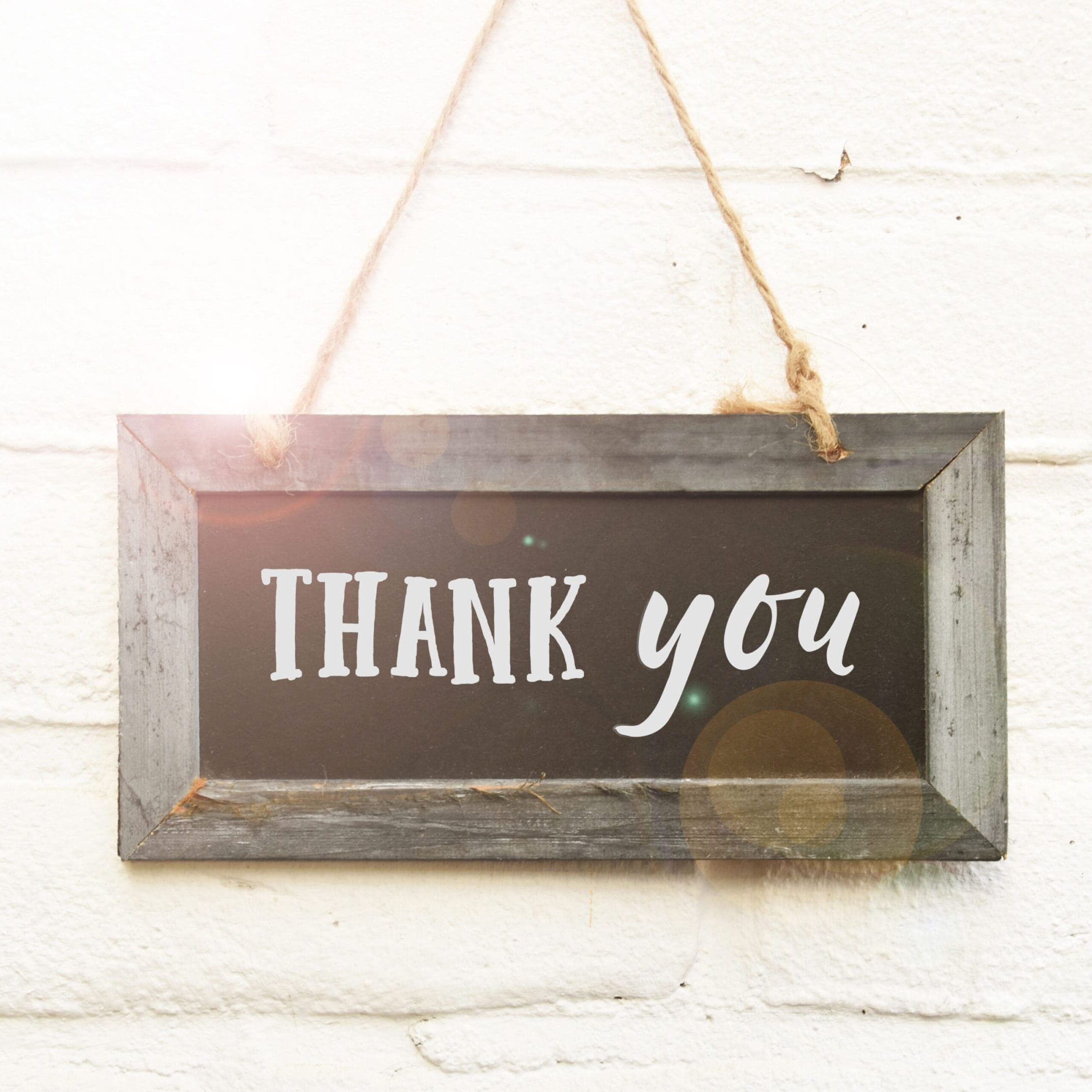 A chalkboard sign that says thank you hanging on a wall.